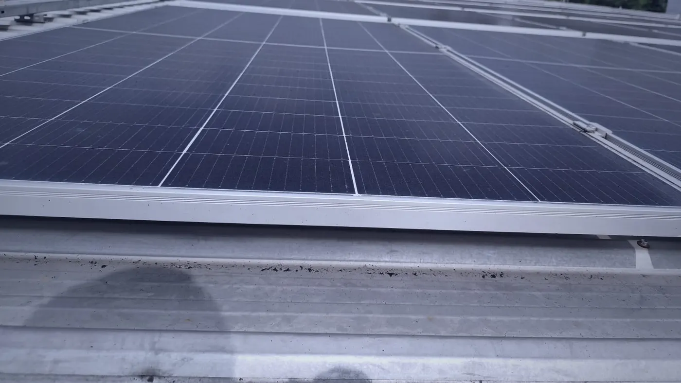 Close-up of a module's mounting rail and clamp against corrugated galvanised iron roof sheeting, showing soiling and staining accumulated along the sheeting below the array